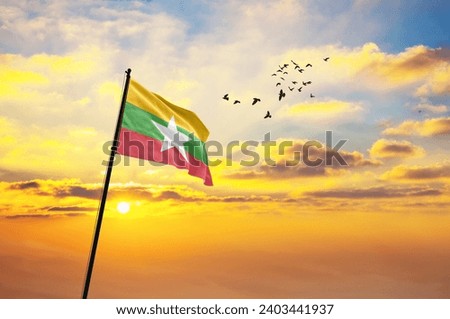 Waving flag of Myanmar against the background of a sunset or sunrise. Myanmar flag for Independence Day. The symbol of the state on wavy fabric. Royalty-Free Stock Photo #2403441937