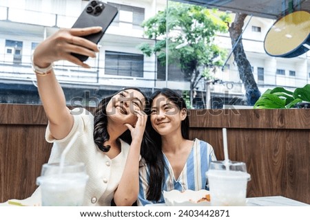 Two young asia females taking selfie using mobile phone while sitting in the cafe, Two joyful attractive Asian girls together at restaurant or cafe. Holiday activity, or modern lifestyle concept
