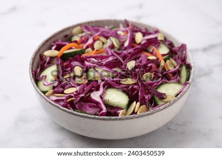 Tasty salad with red cabbage and pumpkin seeds in bowl on marble table, closeup
