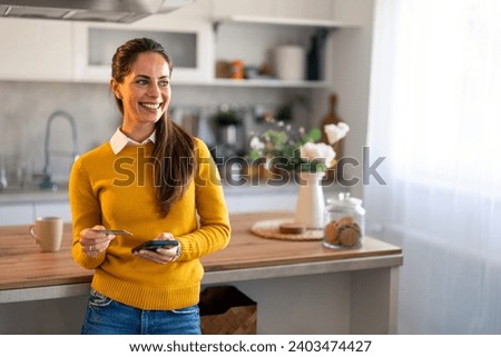 Portrait photo of successful businesswoman looking aside with smile while holding credit card and mobile phone at home.