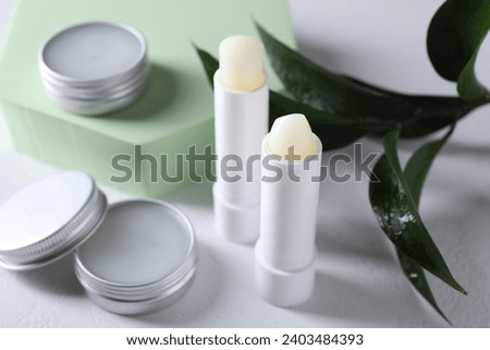 Different lip balms and leaves on white background, closeup Royalty-Free Stock Photo #2403484393