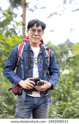 Asian man Photography Camera Nature Environment Concept. Happy asian male backpacker traveling alone in forest wild. Man traveler with camera look around and explore while walk in nature wood.