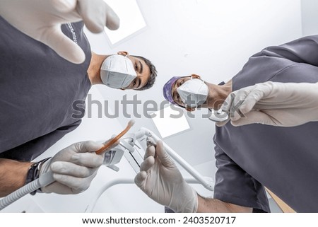 From below male dentist with mirror and probe and assistant with suction device bending over patient during appointment in dental clinic Royalty-Free Stock Photo #2403520717