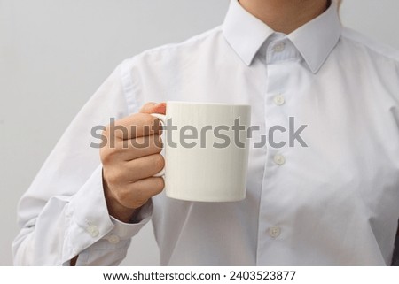 A woman holds a white cup in her hands