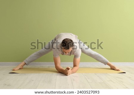 Mature man practicing yoga on mat near green wall