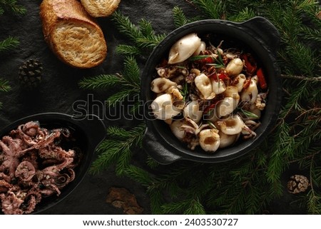 Fried  squid  with chilli pepper, garlic and butter served in iron cast pan on black textured background decorated with forest details. Christmas food decoration concept