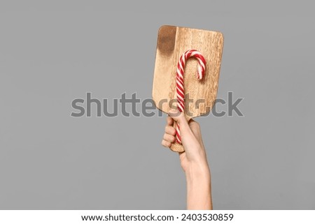 Female hand with wooden cutting board and candy cane on grey background