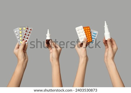 Female hands holding pills in blister packs and bottles of nasal spray on grey background