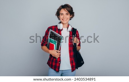 Beautiful, smiling, smart and modern female student with headphones, backpack, notebooks and books in hands, looking at camera. University, study, school, education, college, classes, learn knowledge.