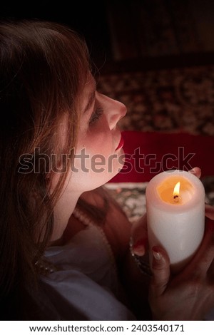 Beautiful arabian girl with candles in red room full of rich fabrics and carpets in sultan harem. Photo shoot of woman an oriental style odalisque. Model poses in sari as a caring wife and hostess