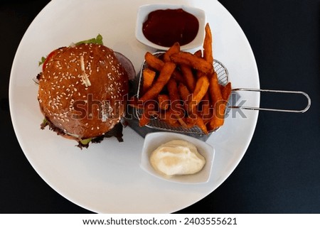 Hamburger with French fries and sauce on a white plate on a black background