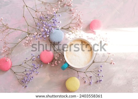  sweet colorful macaroons, cute colorful flowers  and a cup of coffee with milk on a delicate light pink background. Atmosphere of celebration and romance