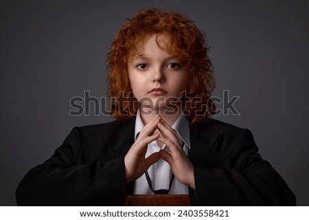 Portrait of a teenage girl with beautiful red curly hair in a black pantsuit with a tie