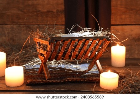 Burning candles and manger with dummy of baby on brown wooden background. Concept of Christmas story
