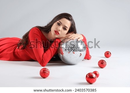Beautiful young woman with Christmas decorations and disco ball lying on grey background