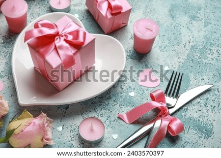 Beautiful table setting for Valentine's Day with pink roses, candles and gifts on blue grunge background