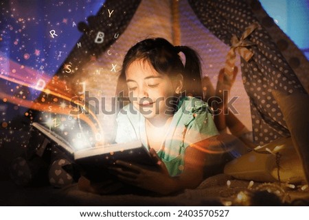 Girl reading shiny magic book with letters flying over it in play tent at home
