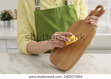 Woman rubbing wooden cutting board with lemon at white table in kitchen, closeup Royalty-Free Stock Photo #2403571843