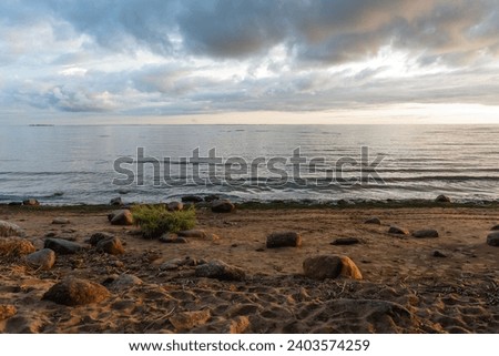 Sea at sunset with big round stones on the shore. The wild coastal nature of the North Sea. The wild coastal nature of the North Sea. Royalty-Free Stock Photo #2403574259