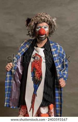 A cheerful curly-haired clown grimaces. Portrait against a background of beige wings. The clown in the parrot tie.