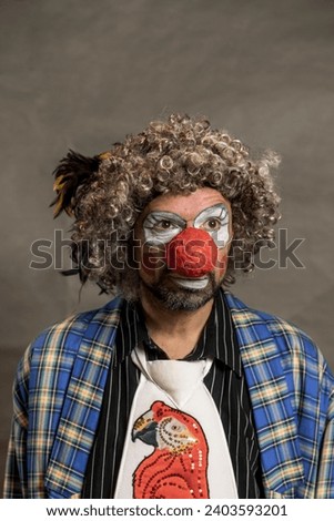 A cheerful curly-haired clown grimaces. A close-up portrait against a background of beige wings. The clown in the parrot tie.