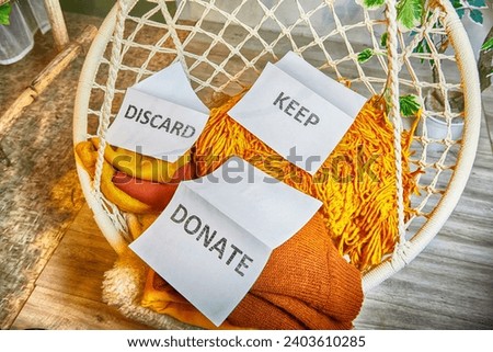 Signs with the words keep, donate, discard and fashion clothes folded in stacks in cozy room. The concept of cluttering and decluttering. Background