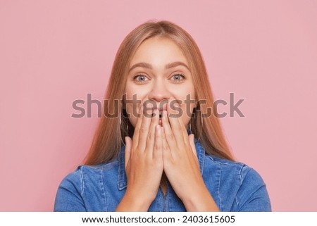 Golden-haired girl in blue denim dress holds hand at her face covering her mouth, good mood concept, copy space. Royalty-Free Stock Photo #2403615605