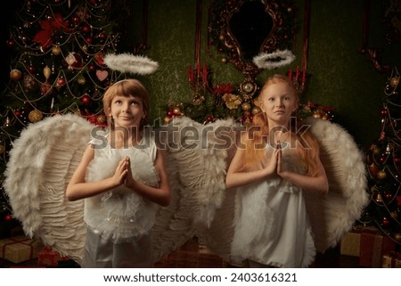 Two little kids dressed as angels  stand in a beautiful Christmas setting and pray. Merry Christmas and Happy New Year! Vintage style.