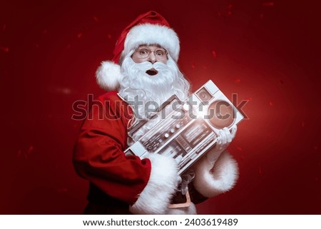 Party for Christmas and New Year. Modern cheerful Santa Claus singing and dancing with a boombox on a red holiday background. Royalty-Free Stock Photo #2403619489