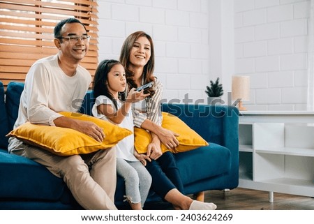An Asian family is joyfully bonding watching TV at home on the sofa. The father mother son and daughter share togetherness relaxation and happiness during their weekend time.