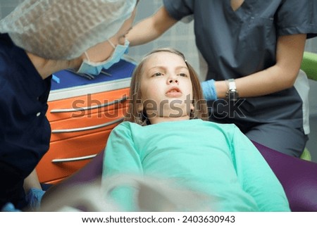Little scared girl sitting in chair in dentist doctor office. Kid,child afraid of tooth extraction, teeth treatment, examine with open mouth. Dental clinic check-up. Reclined position. Dentist gloves.