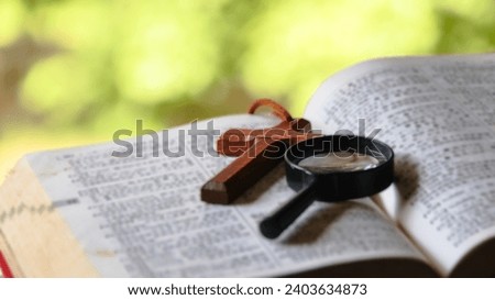 Black magnifying glass and brown wooden cross on blur old book