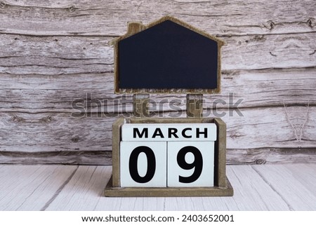 Chalkboard with March 09 calendar date on white cube block on wooden table.