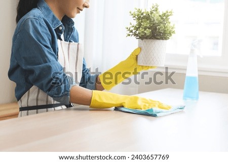 Cleaning hygiene asian young woman wearing protection rubber yellow gloves while clean up holding flower pot take out from table, using blue rag wiping with spray remove dust, housekeeping in room. Royalty-Free Stock Photo #2403657769