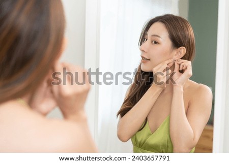 Get dress, elegant asian young woman with makeup glamour, getting ready wearing green cloth, gorgeous female putting earring or jewelry looking into the mirror at home, prepare going event night party Royalty-Free Stock Photo #2403657791