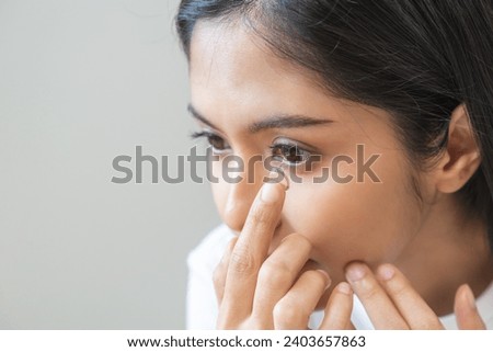 Ophthalmology care, eye sight or vision. Closeup asian young woman, female hand holding and putting, wearing soft contact lens on face with finger, look into eye on background. Medicine and health. Royalty-Free Stock Photo #2403657863