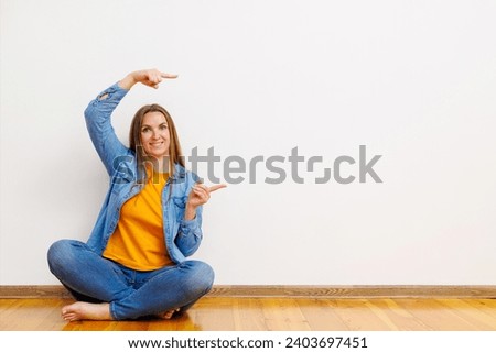 Woman sitting on the floor over white wall pointing with two hands to the side