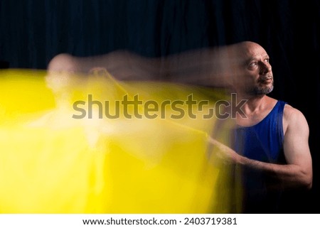 Man, dancer actor making fast movements with yellow cloth. Blurred movements.