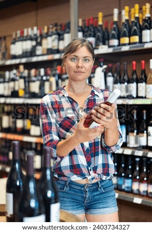 Portrait of young woman visiting winehouse in search of bottle of good wine Royalty-Free Stock Photo #2403734327