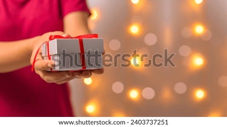 Woman s hands holding beautifully wrapped gifts Christmas gift box. Christmas and New Year lights. Merry Christmas celebration and Happy New Year 2024