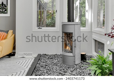 Contemporary Living Room with Standalone Glass Fireplace and Pebble Bed by Large Windows Overlooking Trees Royalty-Free Stock Photo #2403741173