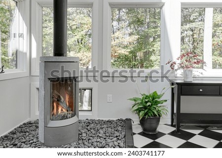 Contemporary Living Room with Standalone Glass Fireplace and Pebble Bed by Large Windows Overlooking Trees Royalty-Free Stock Photo #2403741177