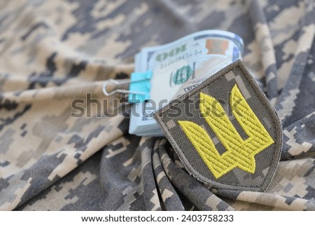 Ukrainian army symbol and bunch of dollar bills on military uniform. Payments to soldiers of the Ukrainian army from United States, salaries to the military. War support to Ukraine