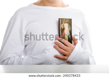 A Caucasian boy holds resting on his chest a picture of Merciful Jesus