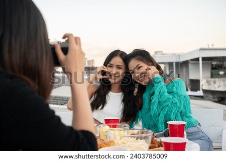 Group of happy young Asian friends partying on a rooftop bar restaurant, having fun and taking pictures together. celebration and city life concepts