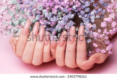 Female hands with pink nail design  hold gypsophila flowers. Pink nail polish manicure on pink background Royalty-Free Stock Photo #2403798261