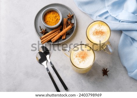 Turmeric golden milk latte with spices and honey. Detox, immunity boosting, anti-inflammatory, healthy, cozy drink in a glass cup on a light background with blue napkin. Top view. Royalty-Free Stock Photo #2403798969