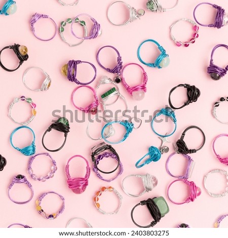 Multicolored handmade rings made of wire and natural stones scattered on a pink background. 