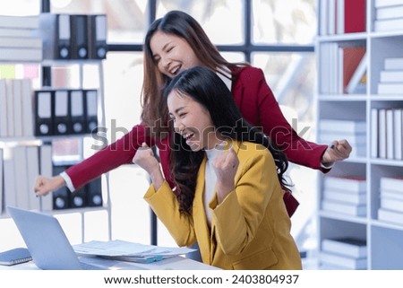 Happy Asian businesswomen working together online on a laptop in corporate office.