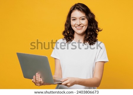 Young Caucasian IT woman she wear white blank t-shirt casual clothes hold use work on laptop pc computer chatting online isolated on plain yellow orange background studio portrait. Lifestyle concept